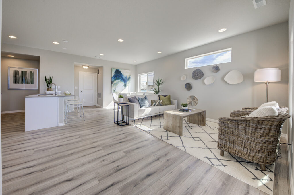 Bright open living area with light wood floors, neutral sofa, wicker chairs, and decorative wall plates.