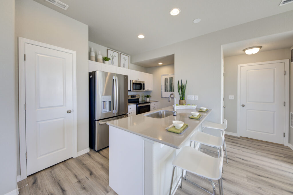 Bright modern kitchen with island, stainless steel fridge, and three bar stools.