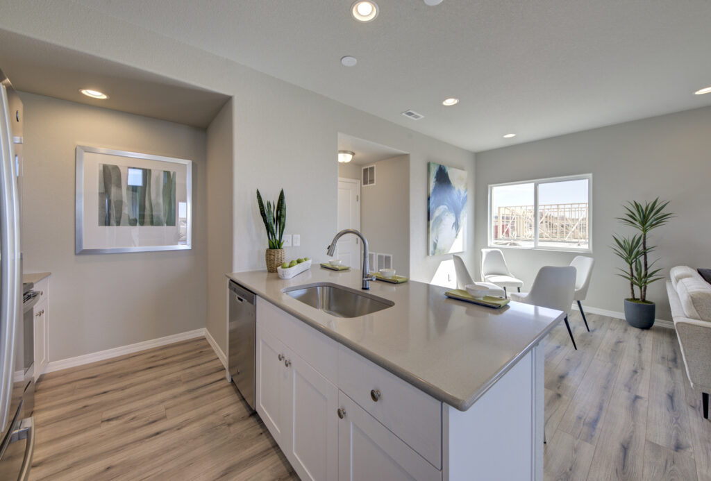 Kitchen island and living area with sink, dishwasher, artwork, and a windowed seating nook.