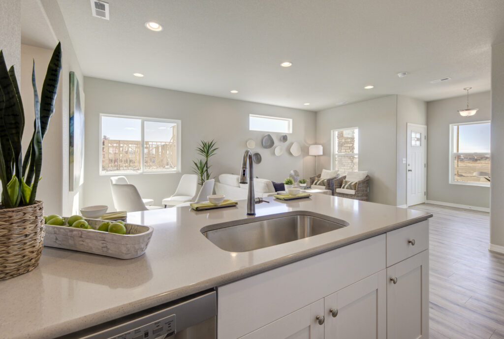 View from kitchen island toward bright living room with large windows and wall decor.