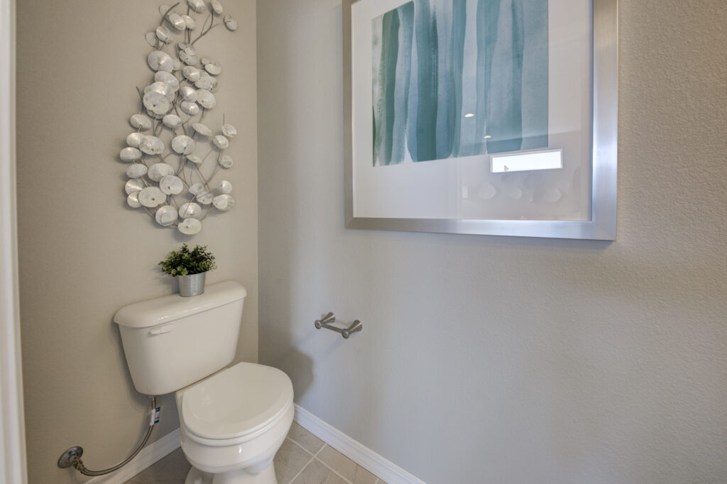 Small toilet room with white toilet, metal wall sculpture, framed abstract print, and a small potted plant on the tank.