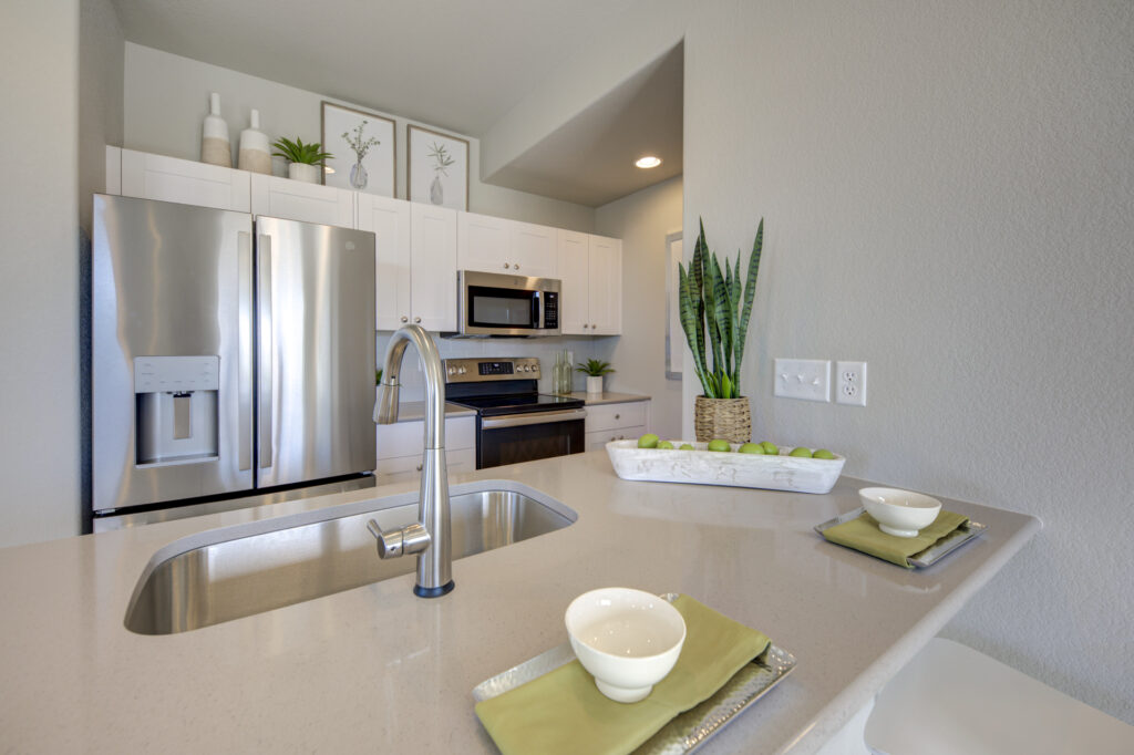 Close-up of kitchen island countertop with sink, faucet, place settings, and stainless fridge behind.