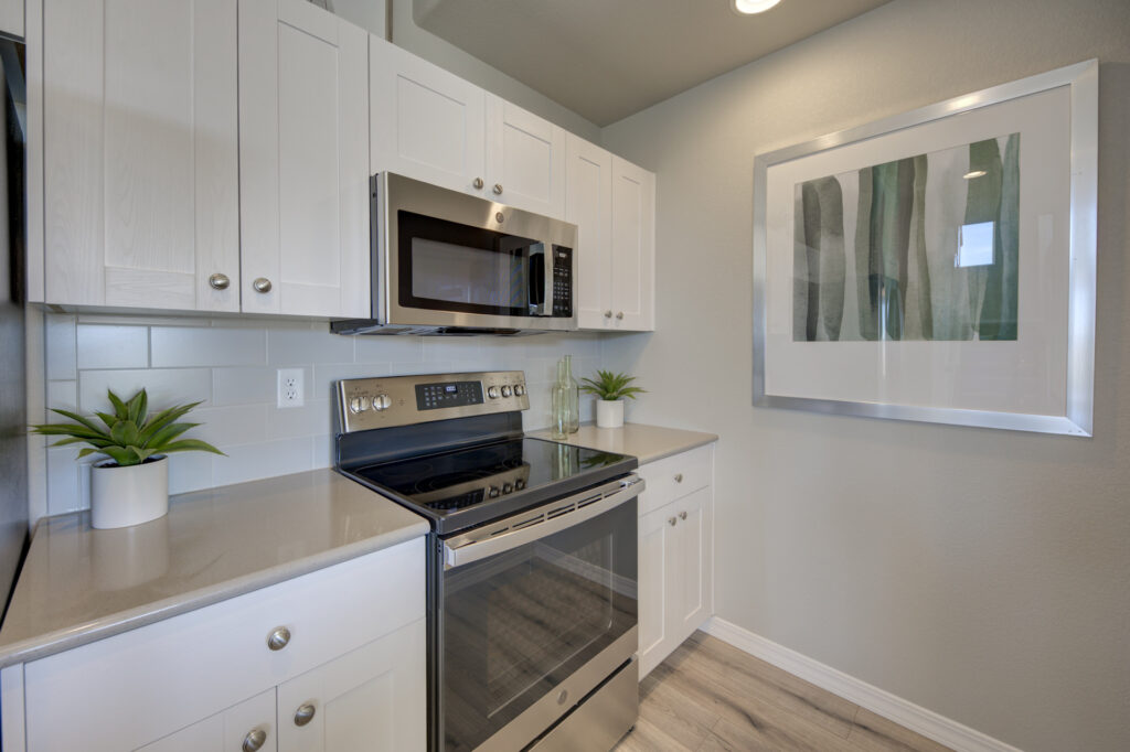 Small kitchen alcove with stainless electric range, over-the-range microwave, white cabinets, and framed artwork.
