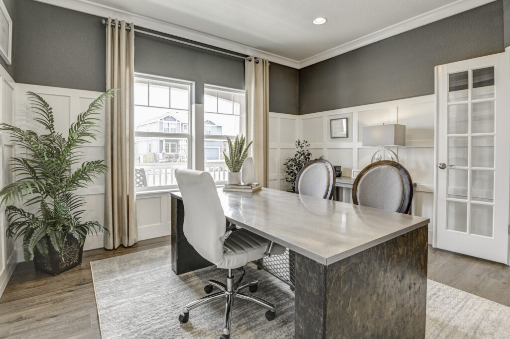Bright home office with large desk, white swivel chair, paneled walls and French-door entry.