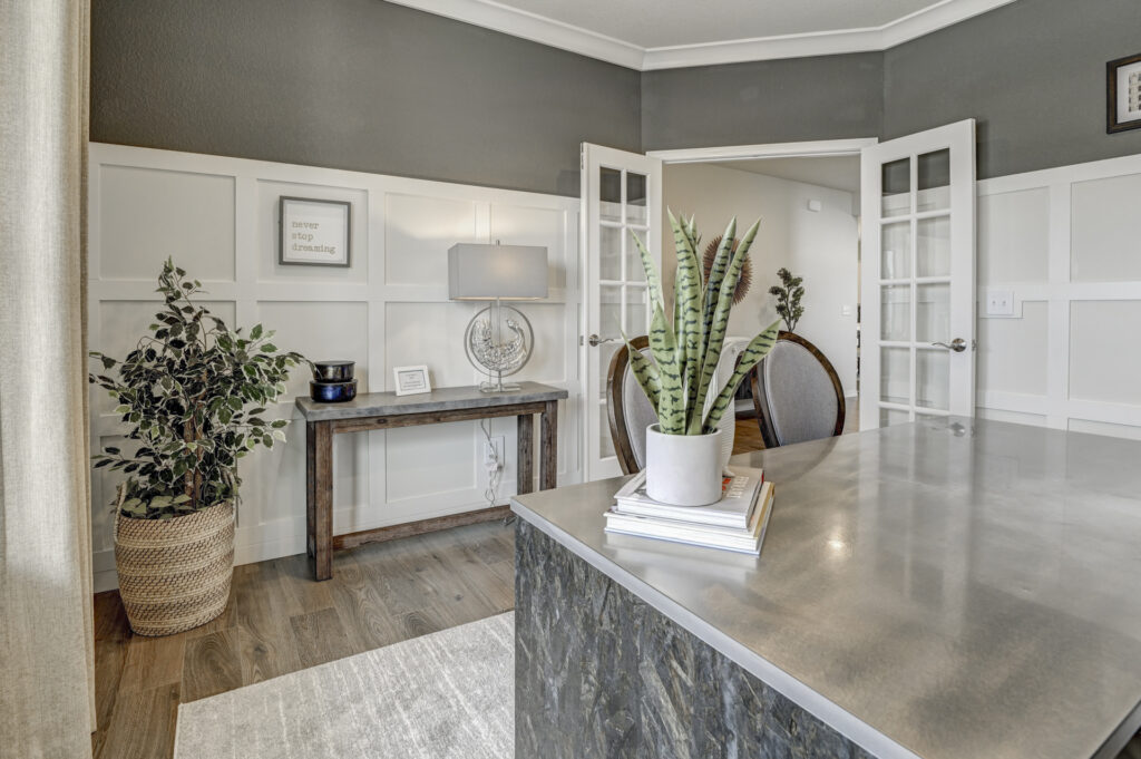 Home office or dining room with wainscoting, double glass doors, and potted plants.