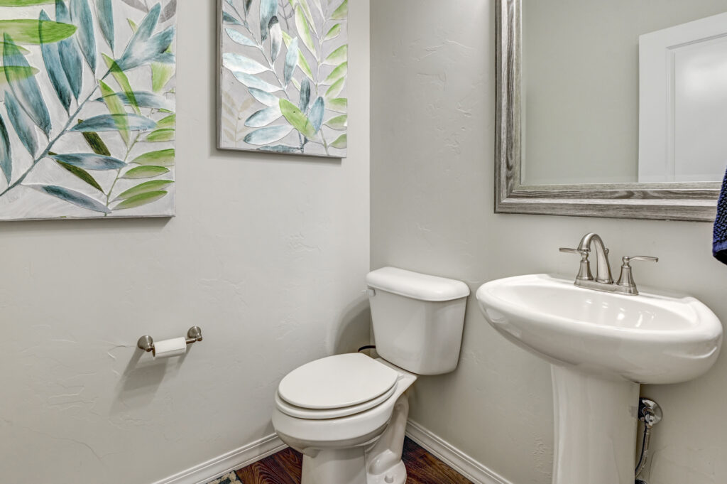 Small half-bath with pedestal sink, toilet, and botanical wall art.