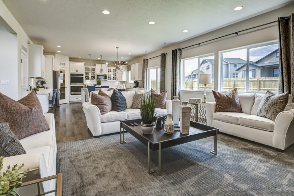 Wide living room view showing sofas, coffee table and large windows overlooking neighboring houses.