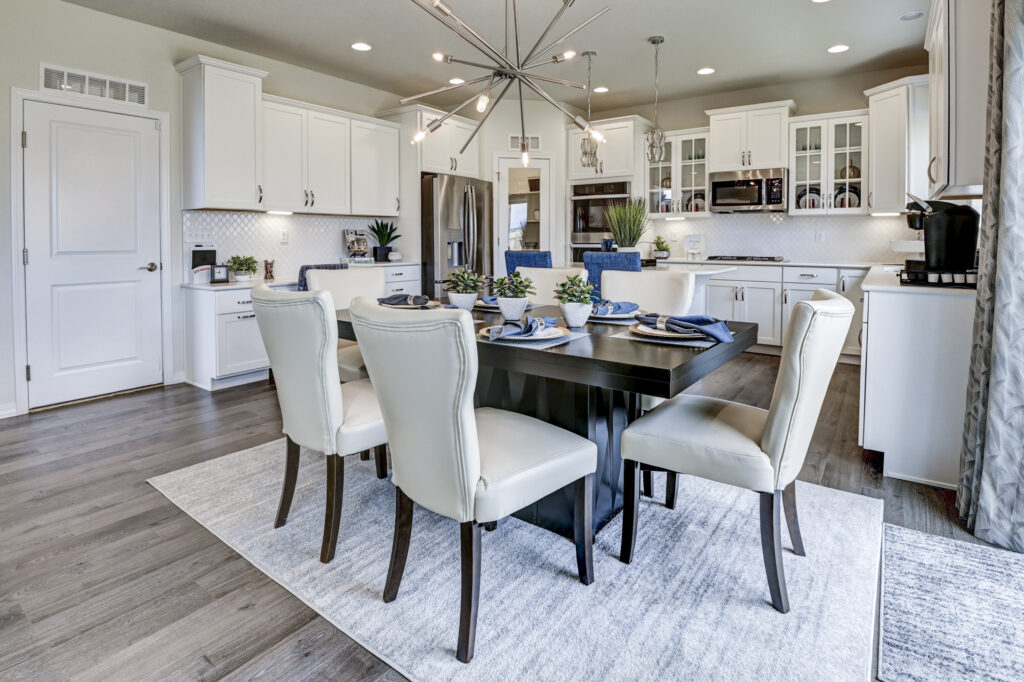 Dining table with six cream chairs in front of a white kitchen with stainless appliances.