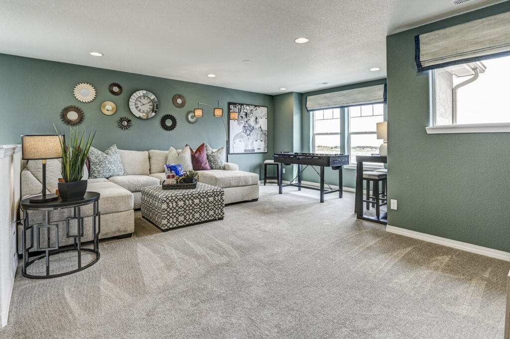Casual living area with sectional sofa, patterned ottoman and teal accent wall decorated with clocks.