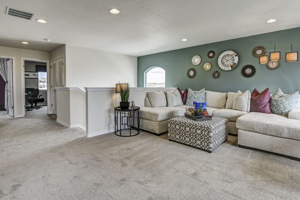 Open upstairs loft with light carpet, sectional sofa and half-wall overlooking hallway.