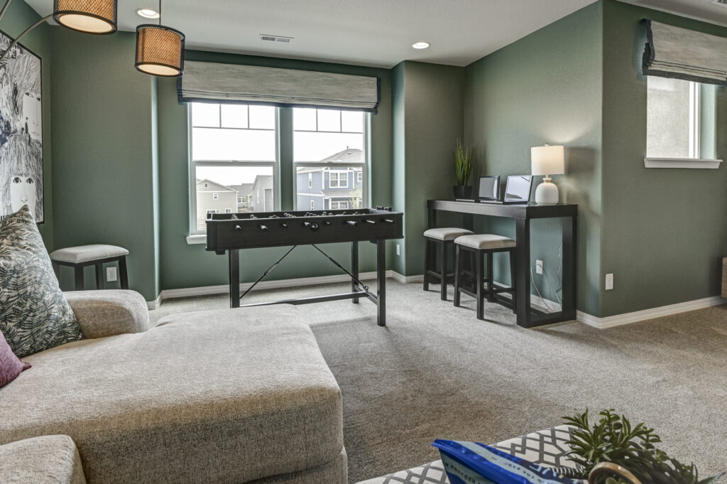 Casual upstairs lounge with green walls, sectional sofa and foosball table near two windows.