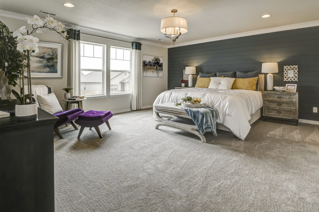 Bright bedroom with dark shiplap accent wall, large bed and purple accent chairs by window.