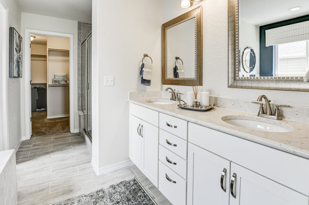 Bright bathroom vanity with double sinks, marble countertop, framed mirrors and tiled floor.