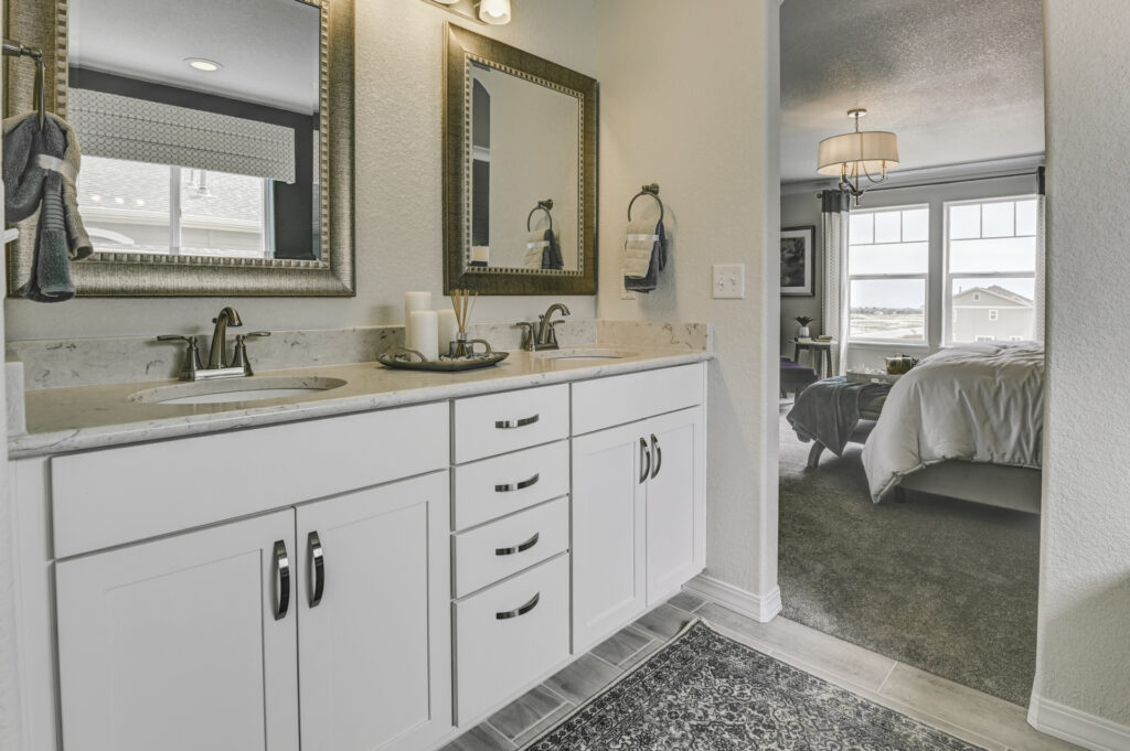 Bathroom vanity with dual sinks and views into a bedroom through an open doorway.