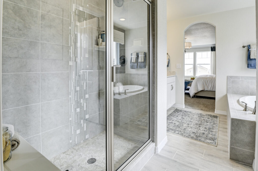 Bright bathroom with glass-enclosed tiled shower and separate soaking tub visible through an arched doorway.
