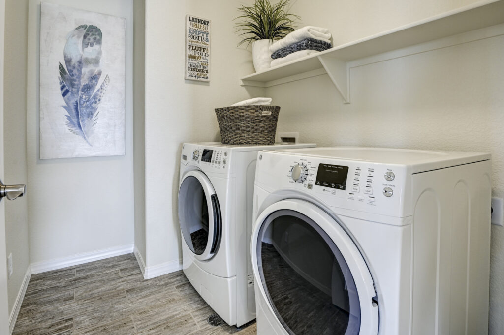 Laundry room with front-loading washer and dryer, shelving, and a decorative basket on top.