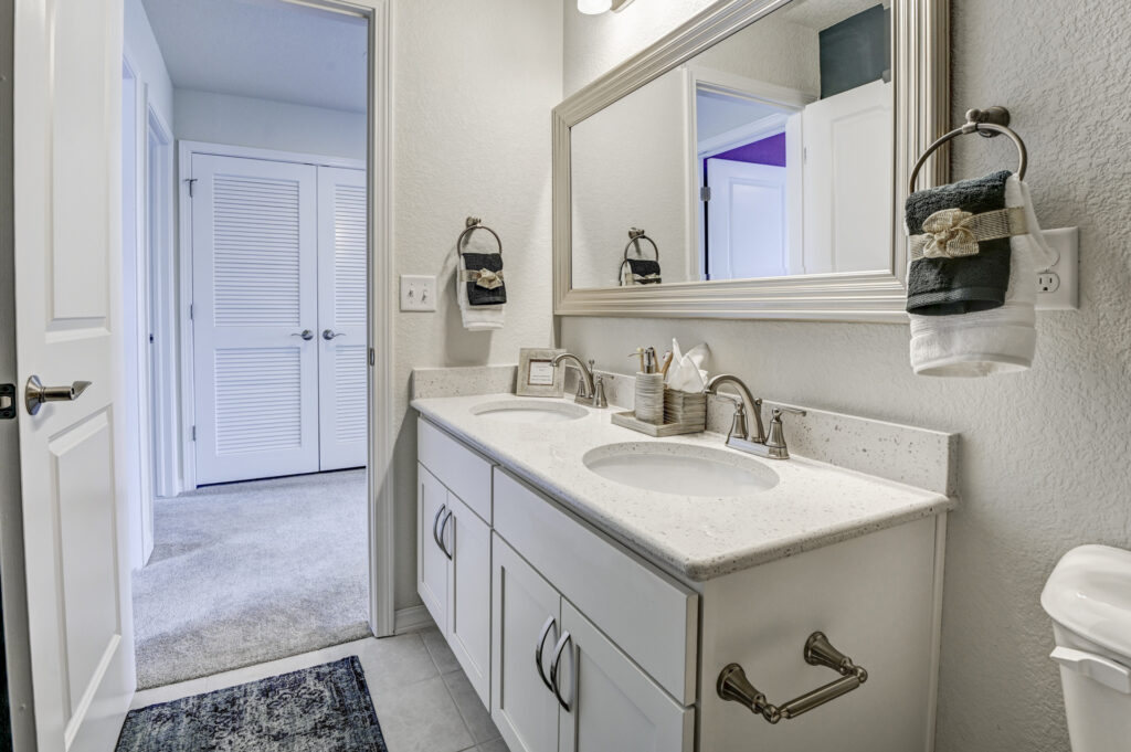 Bright bathroom with double-sink vanity, large mirror, and towel rings on textured walls.