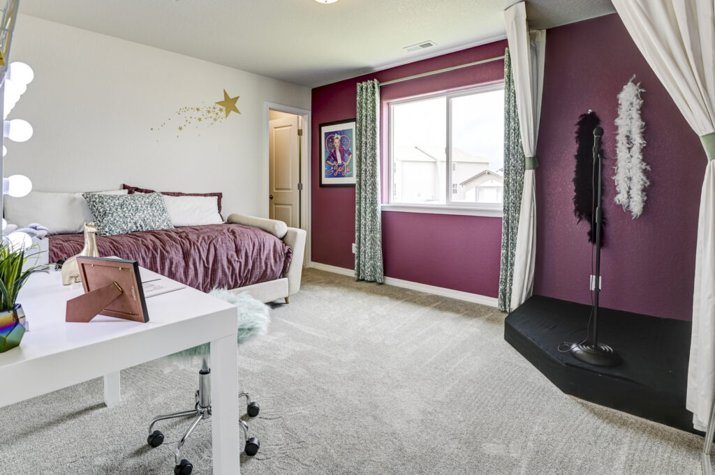 Bedroom with plum accent wall, daybed, vanity desk, and small curtained stage or alcove.