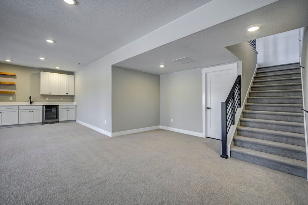 Finished basement living area with wet bar, carpeted floor, and stairway to upper level.