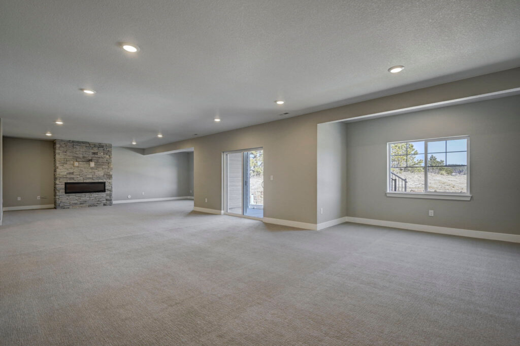 Expansive carpeted room with sliding glass door, windowed alcove and stone fireplace in distance.
