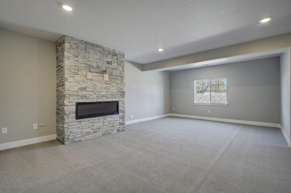 Large carpeted room with stone-clad fireplace and recessed ceiling lights.
