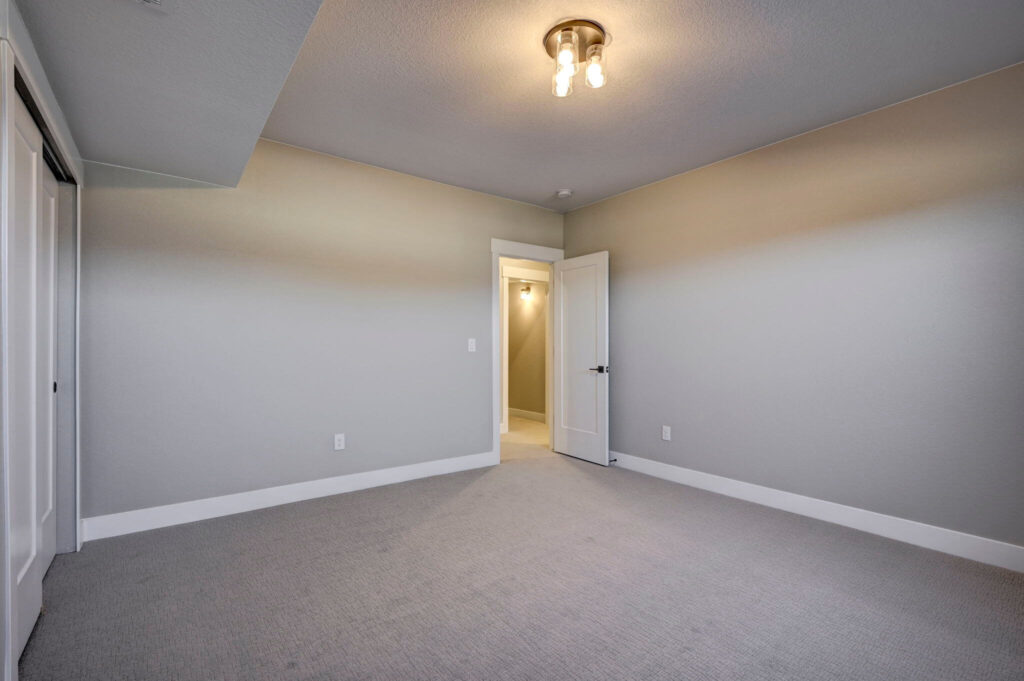 Empty carpeted bedroom with gray walls, white trim, and an open door to a lit hallway.