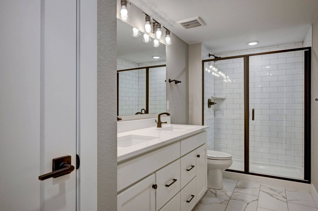 Modern bathroom vanity with double sinks, large mirror, and glass-enclosed tiled shower.