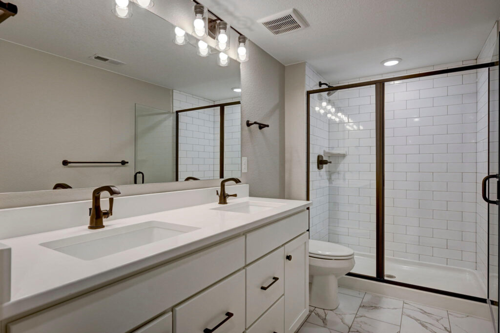 Bright bathroom with dual sinks, long mirror, and a framed glass shower door over subway tile.