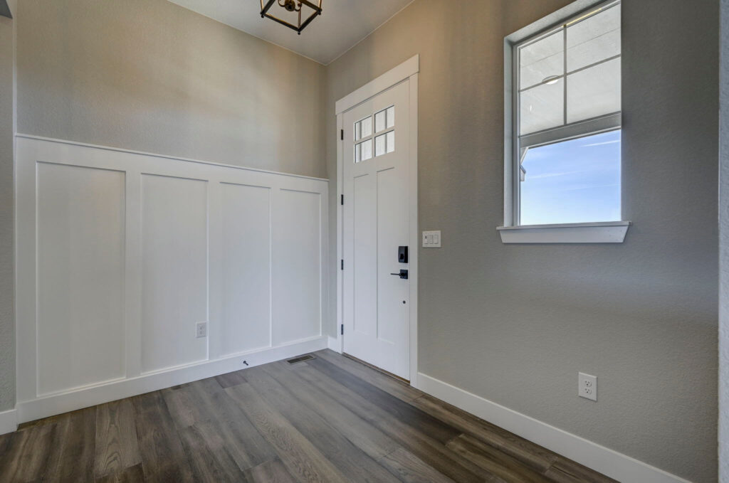 Small foyer with white paneled wainscot, window, and a white entry door with sidelights.