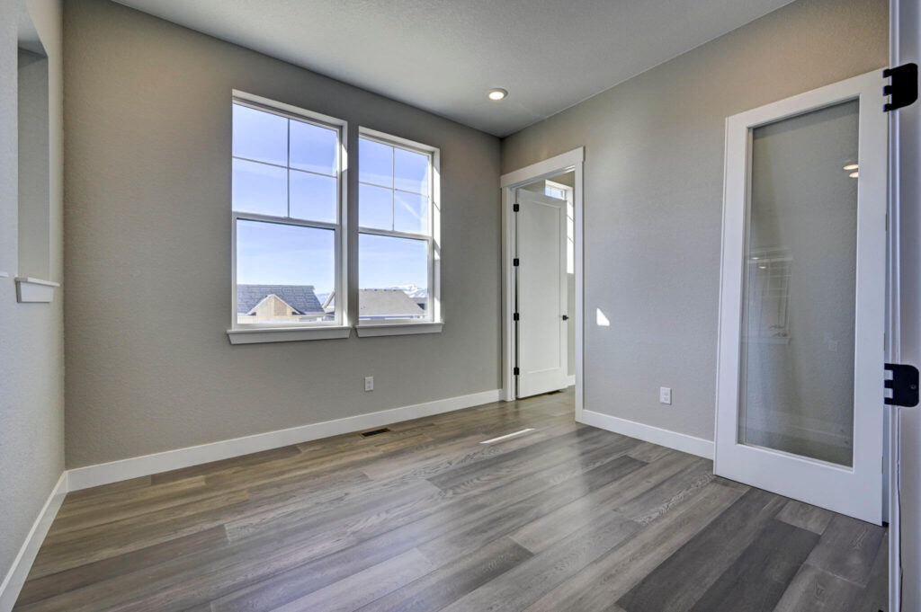 Sunny room with two large windows, gray walls, and a frosted glass interior door leaning open.