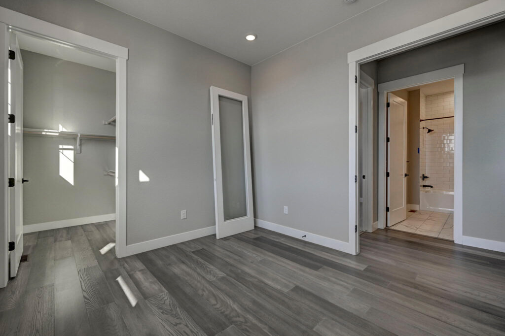 Empty room showing a walk-in closet doorway, a bathroom entry, and a glass-paneled door leaning against the wall.