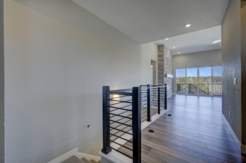 Upper landing or hallway with metal railing, wood-look flooring, and open view to a living area and balcony.