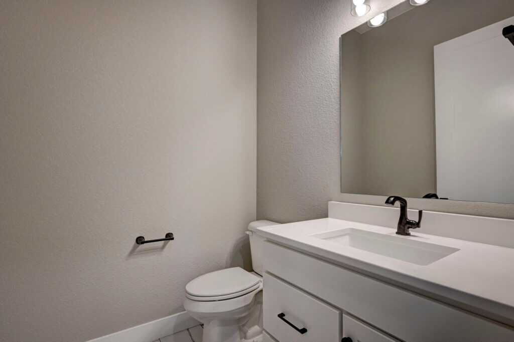 Bathroom sink and toilet against light gray walls with a rectangular mirror and single faucet.