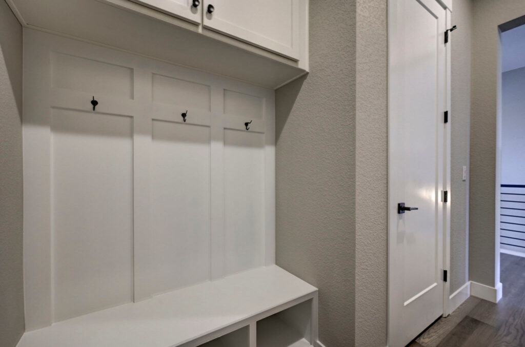 Built-in white cubby bench with three coat hooks and overhead storage cabinets in a hallway nook.