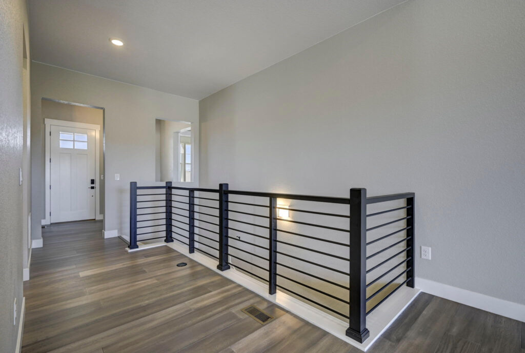 Bright upstairs hallway with metal horizontal-rail banister and wood-look flooring.