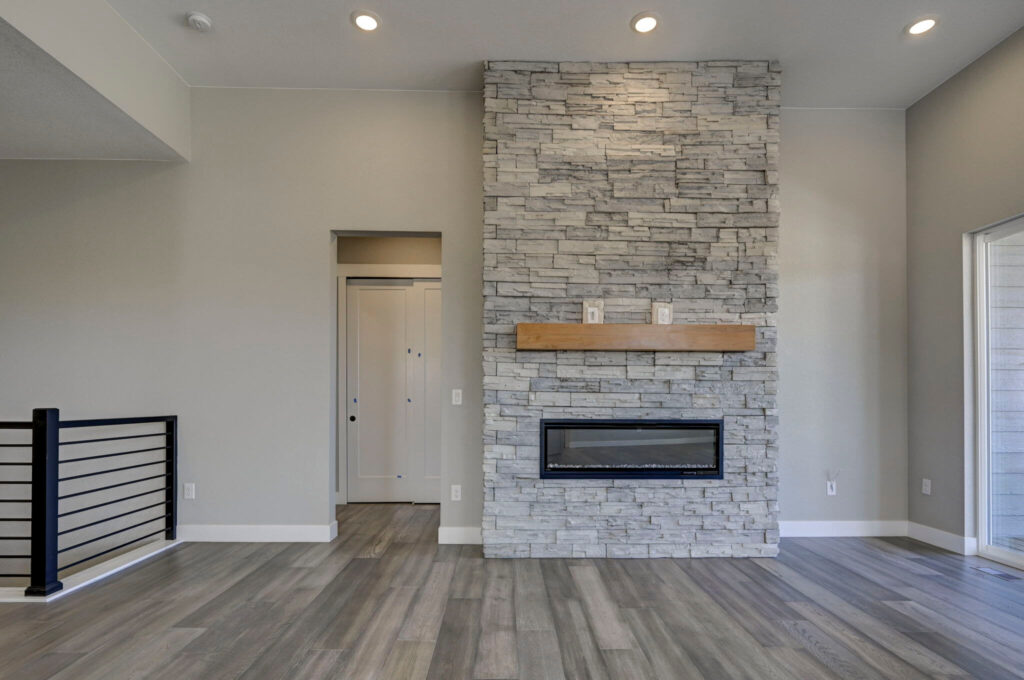 Living area wall with stacked-stone fireplace, wooden mantel, and recessed lighting.