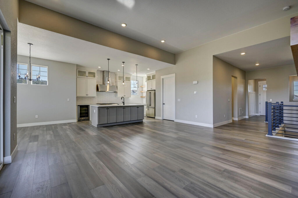 Open-plan living area looking toward kitchen island with pendant lights and wide plank floors.