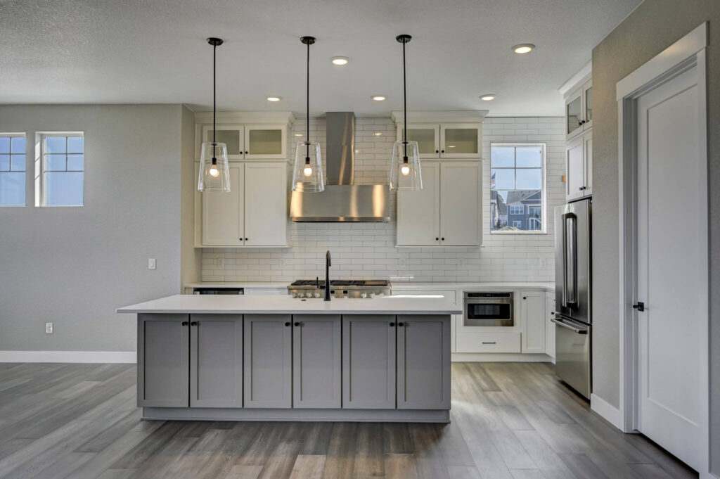 Modern kitchen with large island, pendant lights, subway tile backsplash and stainless range hood.