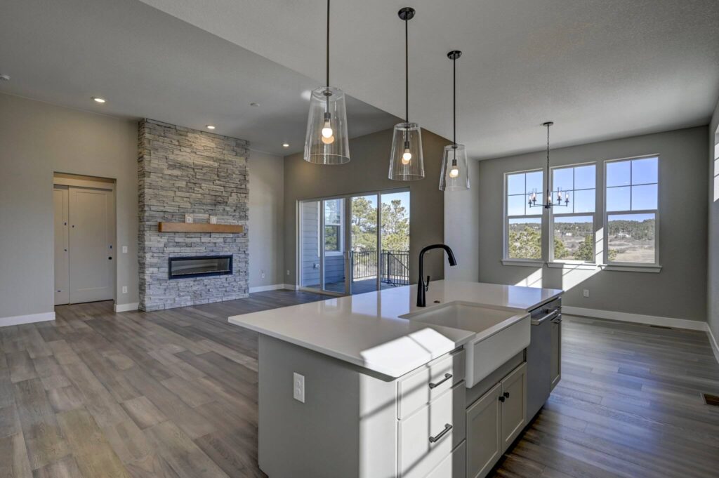 Open-plan living area seen from the kitchen, stone fireplace, sliding doors and dining windows.