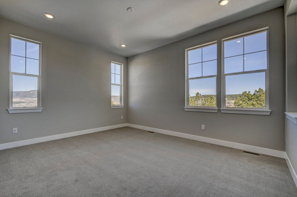Empty carpeted bedroom with multiple windows offering distant hill and tree views.