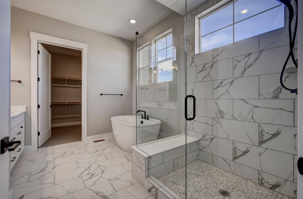 Bathroom with freestanding tub, walk-in glass shower and marble-look tile flooring and walls.