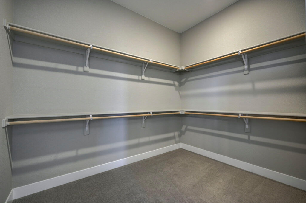 Empty walk-in closet with corner shelving and hanging rods on two walls.
