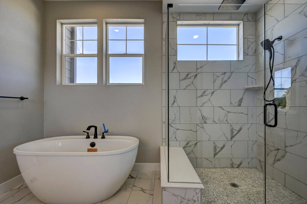 Freestanding bathtub next to a glass-enclosed shower with marble-look tile.