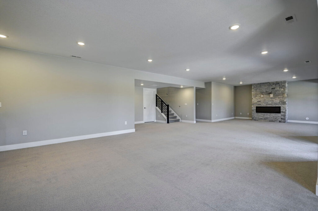 Expansive finished basement with recessed lights, stairway, and stone fireplace at far end