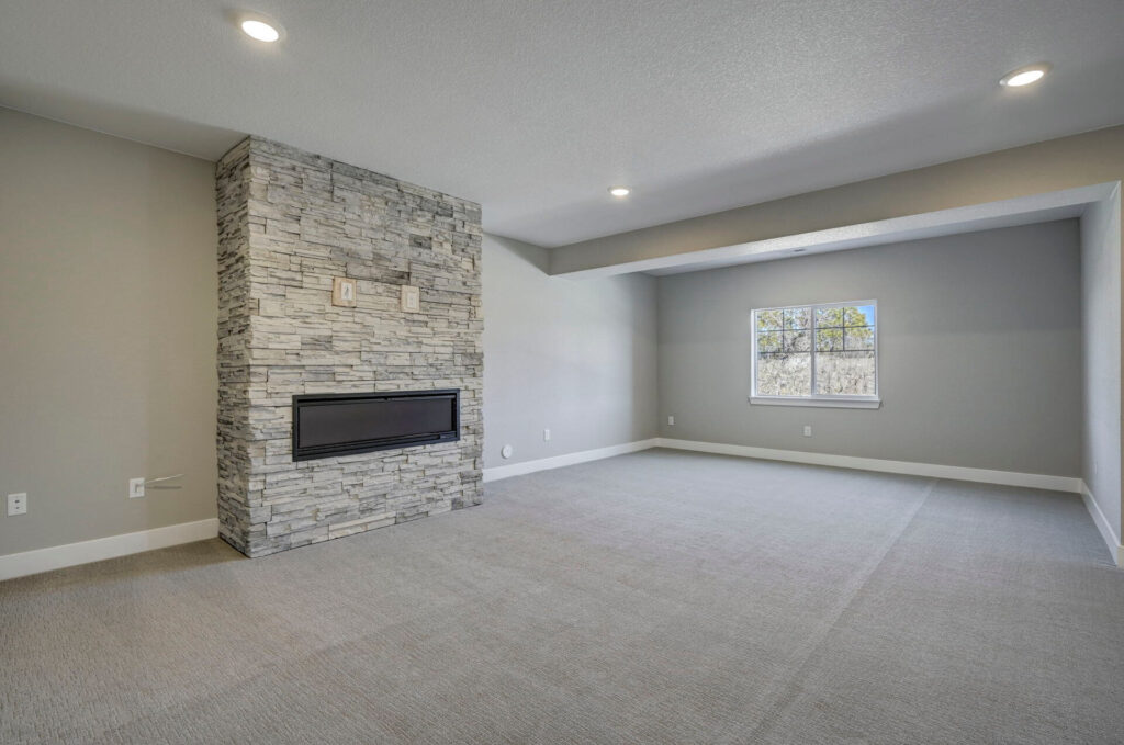 Carpeted room corner showing a stacked-stone fireplace and a recessed windowed alcove.