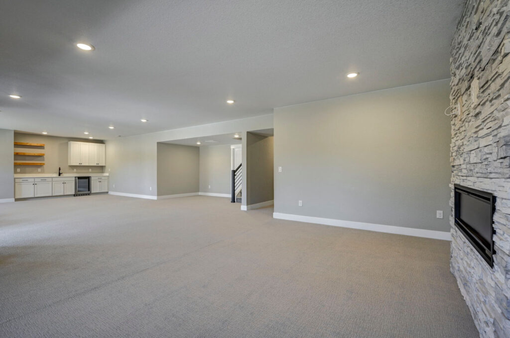 Large open finished basement with built-in wet bar and stone fireplace on right wall.
