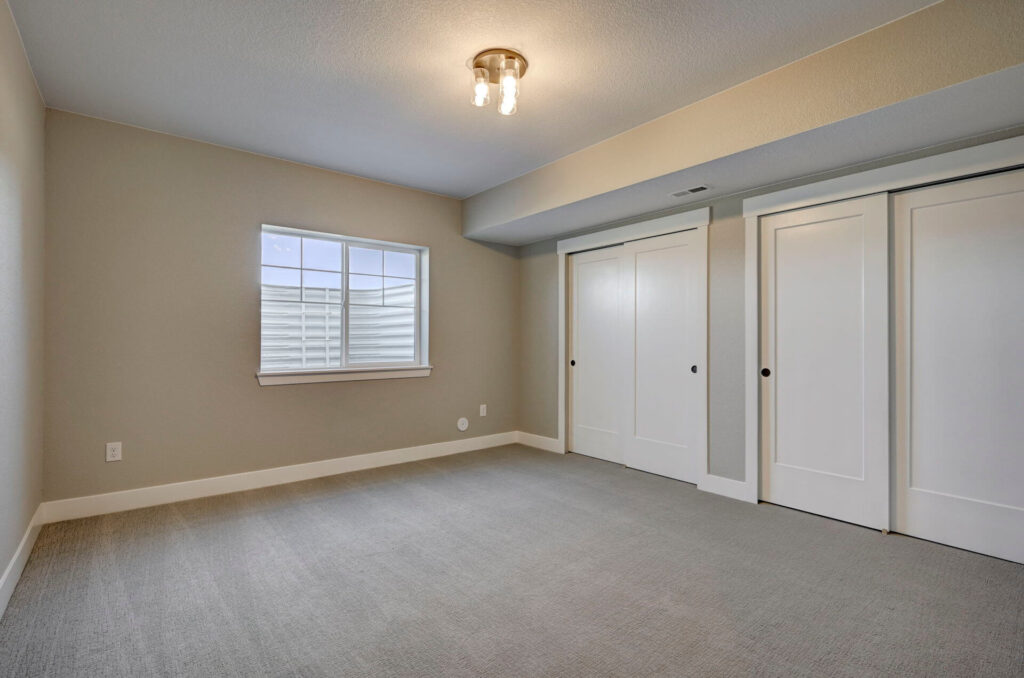 Carpeted bedroom or bonus room with window well and double sliding closet doors.