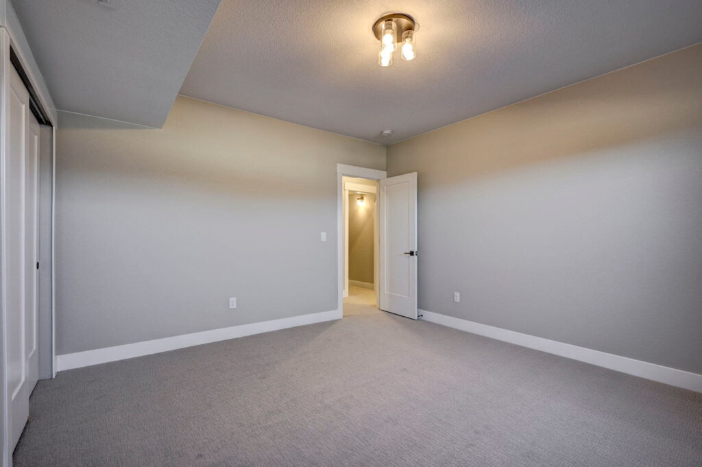 Empty carpeted bedroom with open door to a hallway and overhead light fixture.