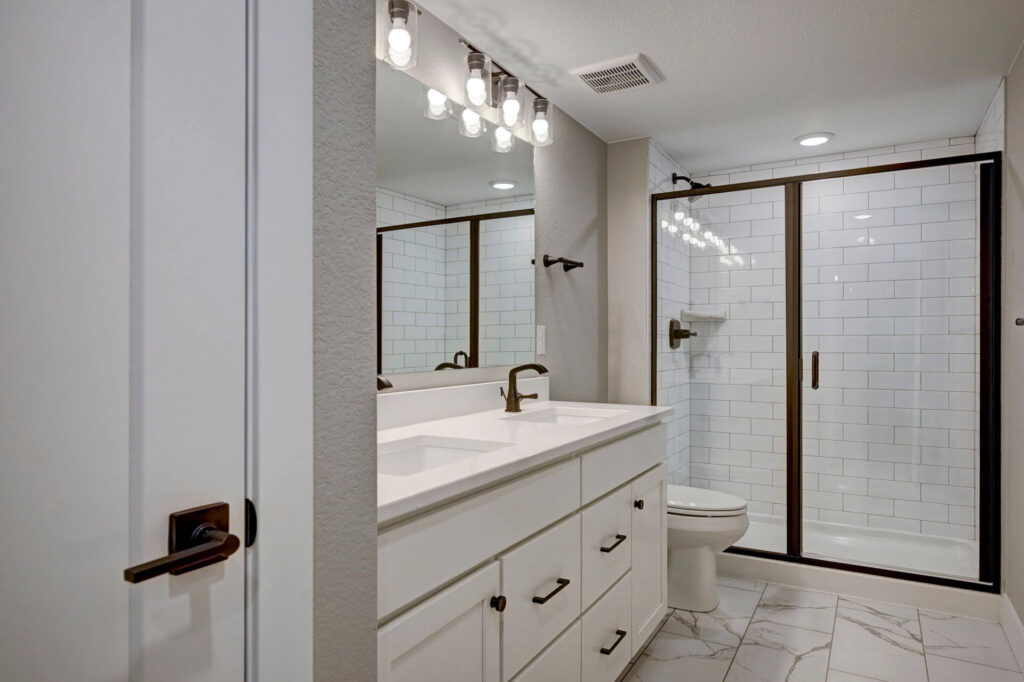 Modern bathroom with double-sink vanity, glass-enclosed shower, and subway tile surround.
