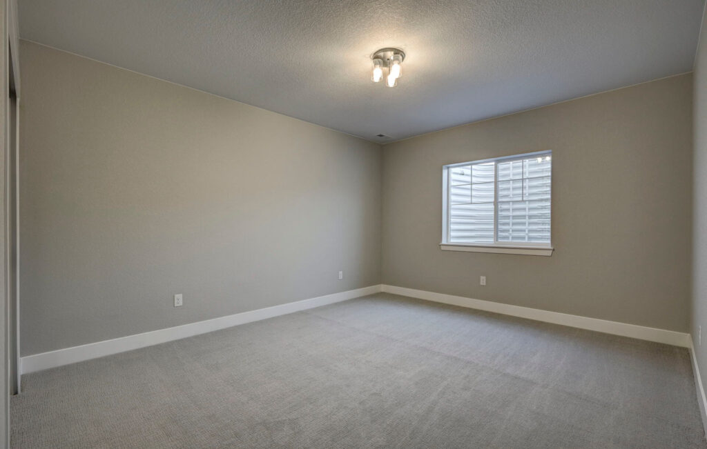 Empty carpeted room with a small window and neutral-colored walls.